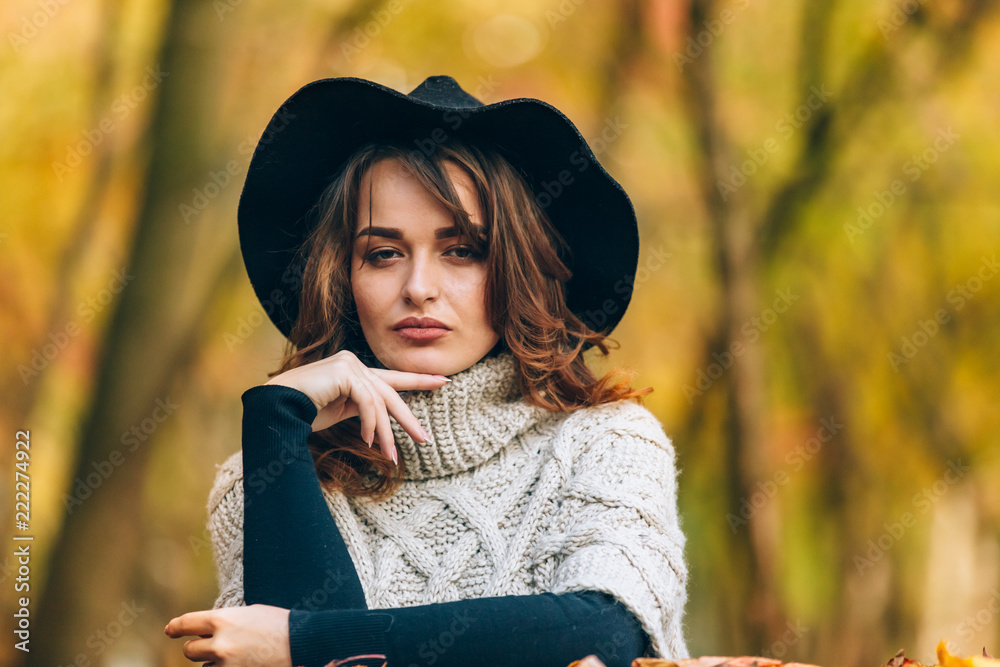 amazing girl in a black hat and knitted sweater holds her hand on the chin and looks at the camera o