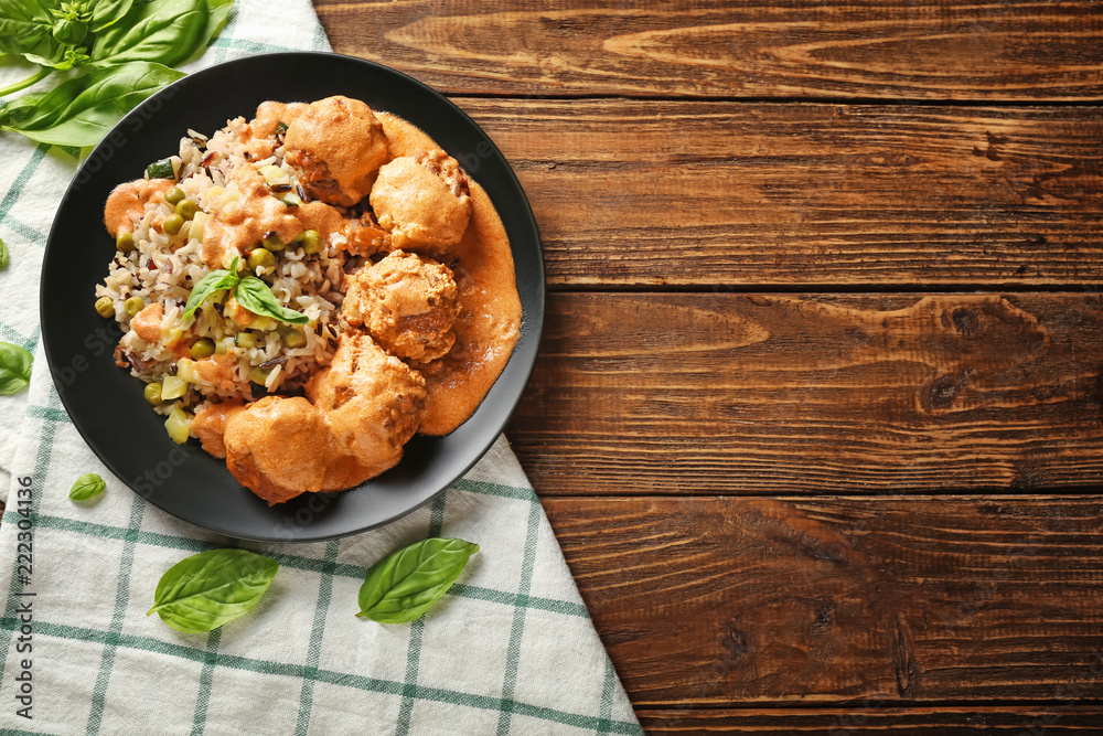 Plate with boiled rice, vegetables and meatballs on wooden table