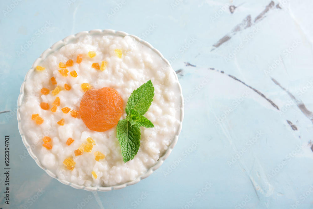 Bowl with delicious rice pudding and dry apricots on color background