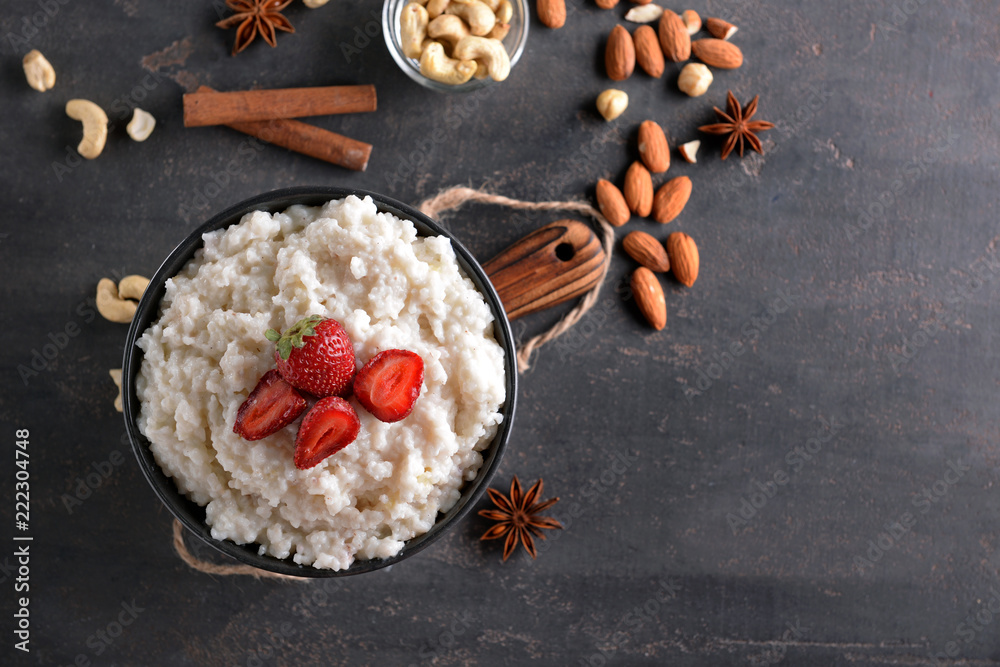 Bowl with delicious rice pudding and strawberry on dark table