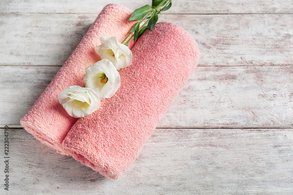 Soft towels with flowers on light wooden table