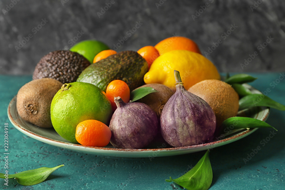 Plate with various delicious exotic fruits on color table