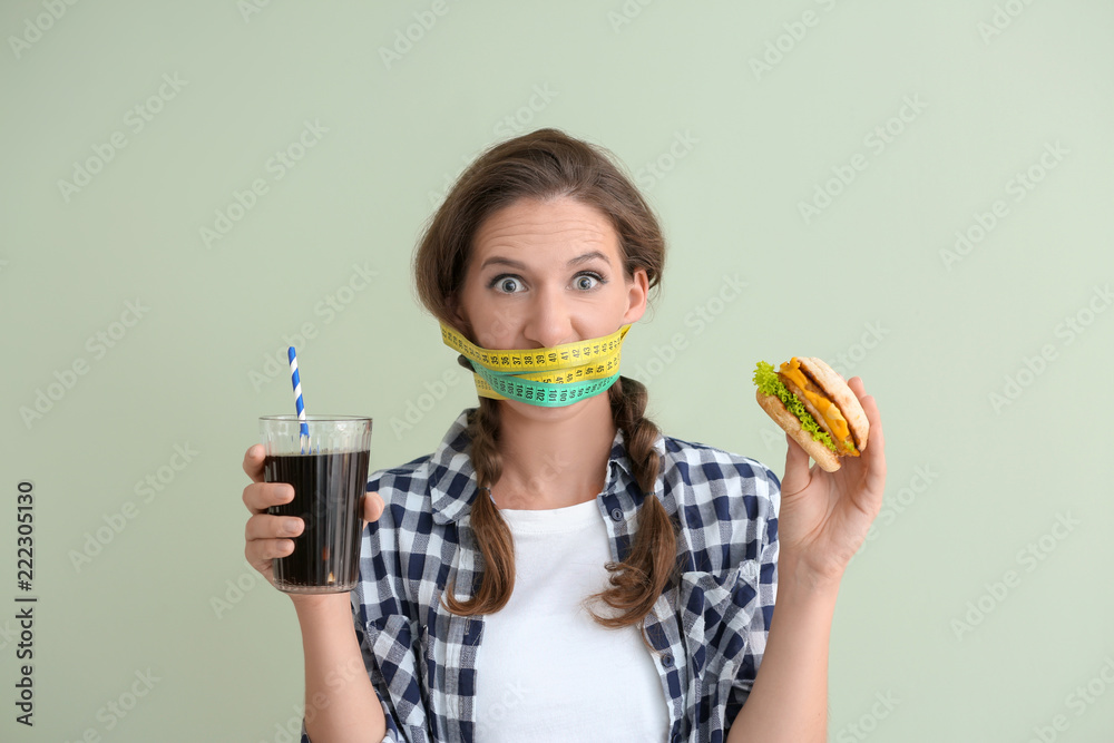 Emotional woman with measuring tapes around her mouth and unhealthy food on color background. Diet c