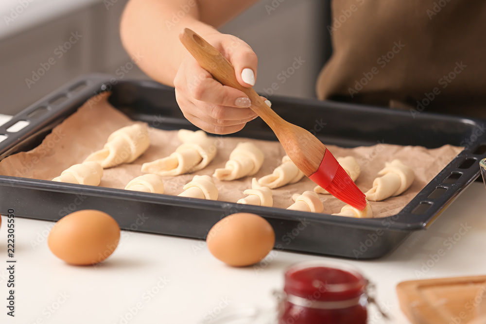 Woman spreading egg yolk on croissants at table, closeup