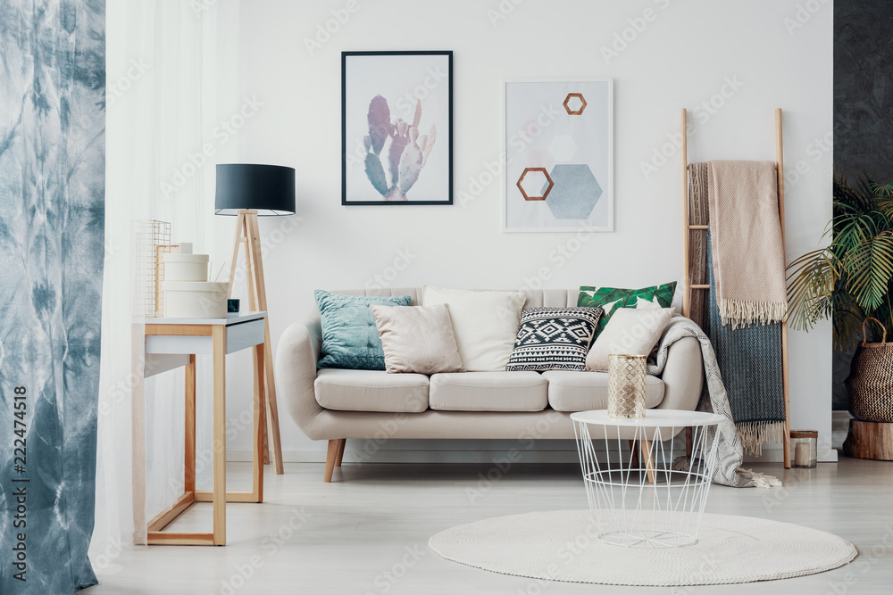 Posters above sofa with pillows in bright living room interior with drapes and round rug. Real photo