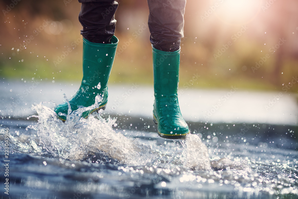 Child walking in wellies in puddle on rainy weather. Boy under rain in summer