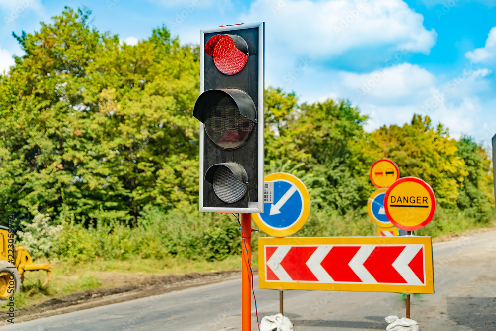 traffic-light stands at the side of the road near the sign of danger in the summer