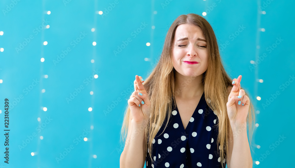 年轻女子交叉手指，在闪亮的灯光背景下祝好运