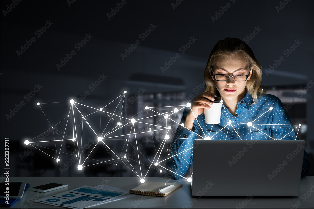 Attractive blonde wearing glasses in dark office using laptop. Mixed media