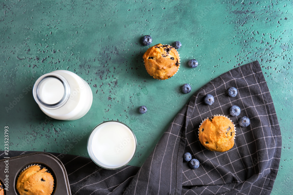 Tasty blueberry muffins with milk on color table