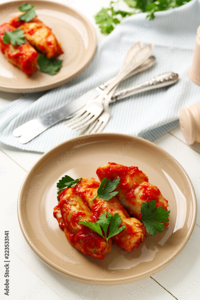 Plate with stuffed cabbage leaves in tomato sauce on white table