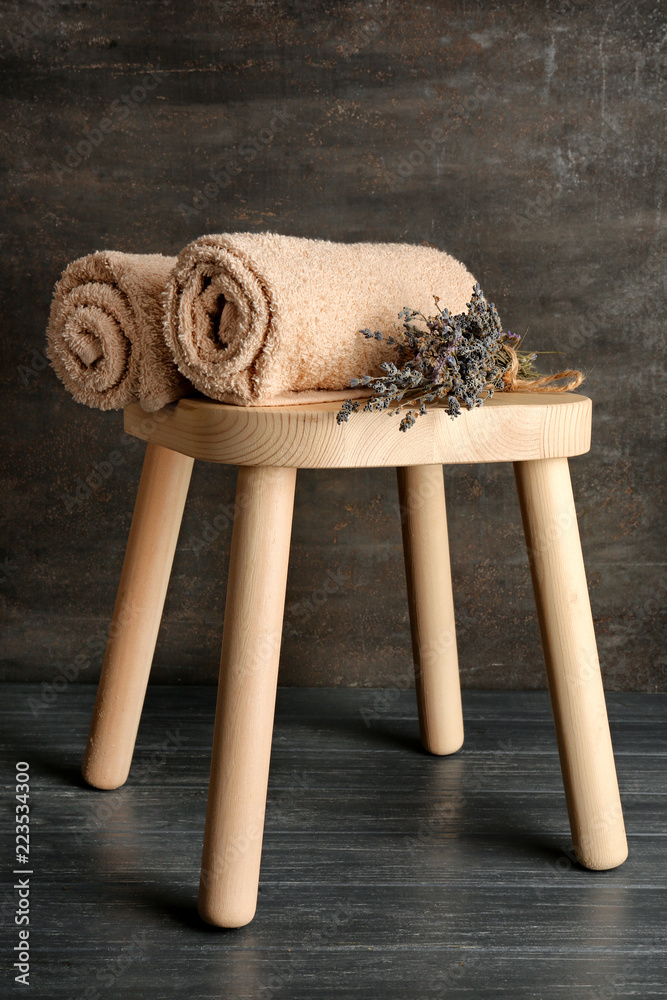 Wooden stool with soft towels and dry lavender on dark background