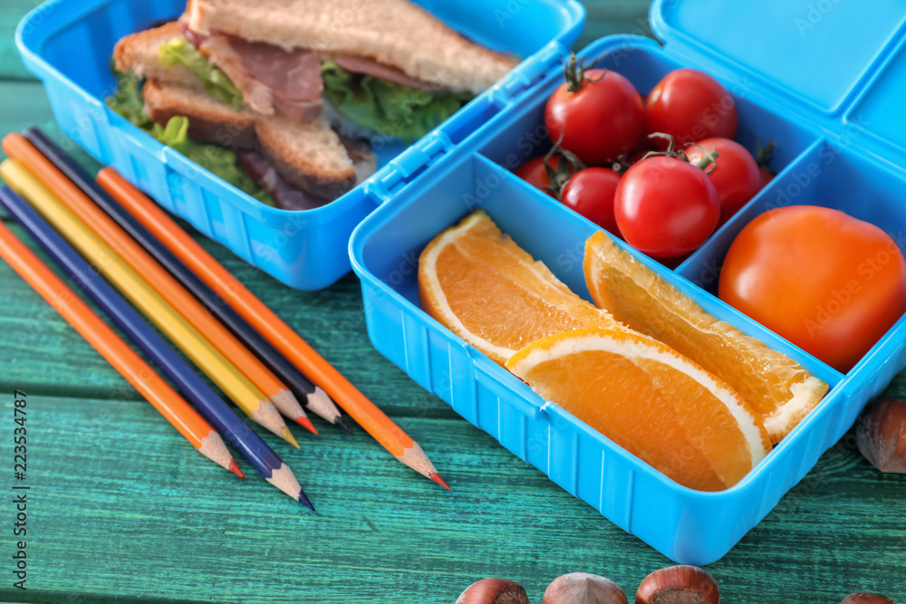 Lunch box with appetizing food and stationery on color wooden table