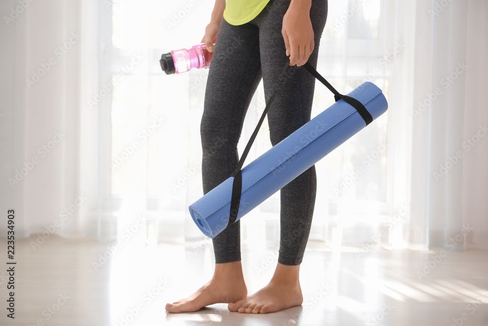 Young woman with yoga mat indoors