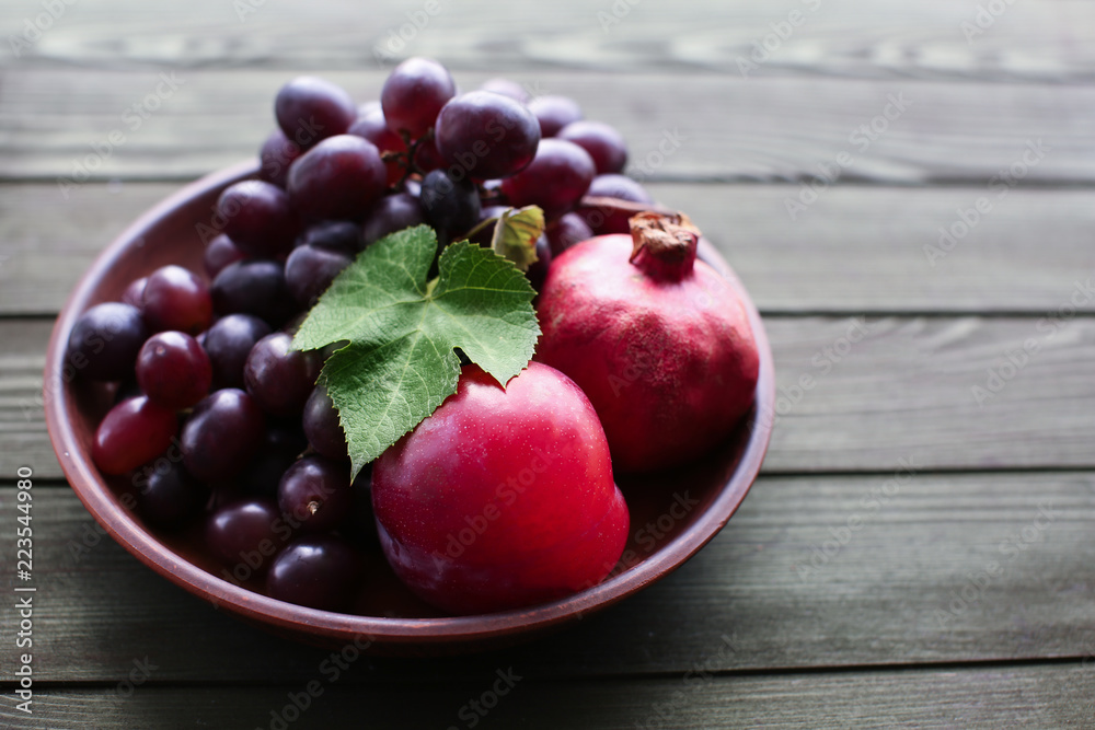 Plate with sweet grapes and pomegranates on wooden table