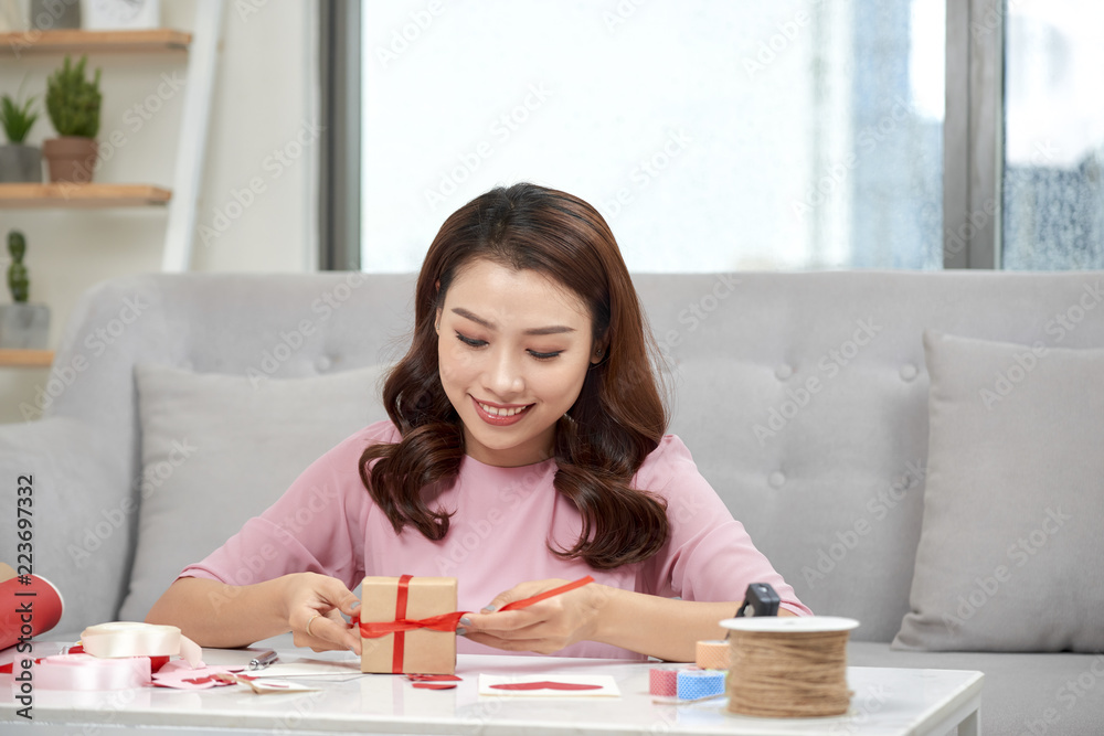 一步一步，微笑的亚洲女人在客厅背景上包装节日礼物