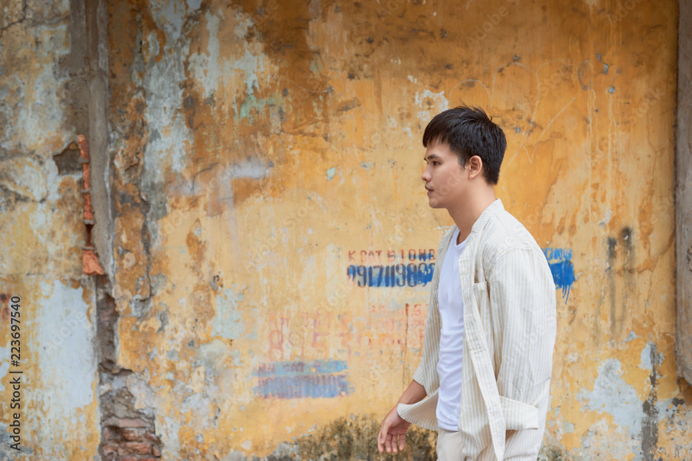 Asian man in casual clothes  standing on old wall background.