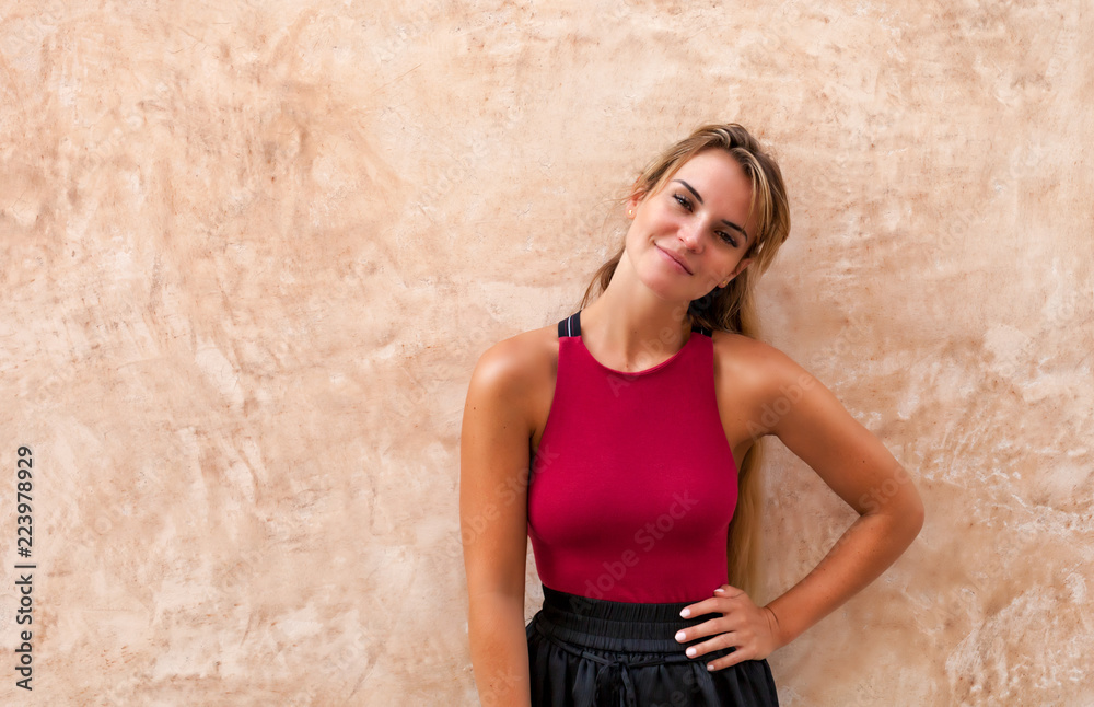 Cheerful beautiful young woman posing against wall on the street