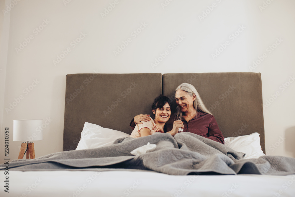 Happy mother and daughter sitting together on bed at home