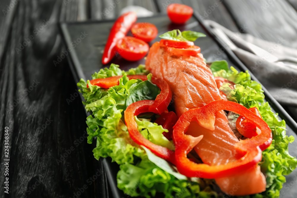 Plate with tasty salmon and fresh salad on wooden table