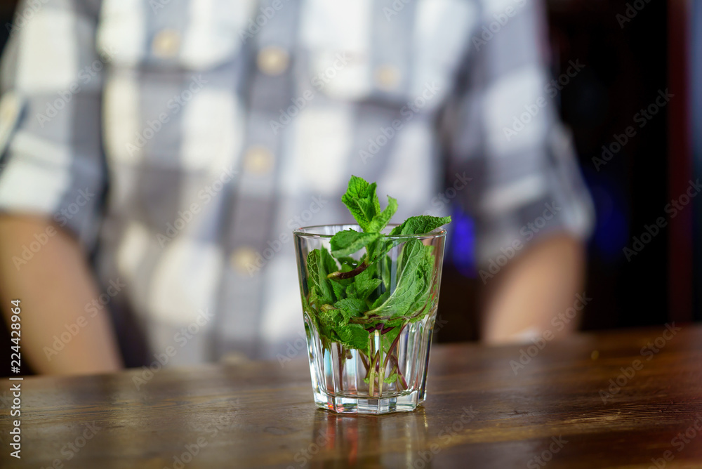 a glass filled with branches of a fragrant mint standы on a wooden table on the background of a man 