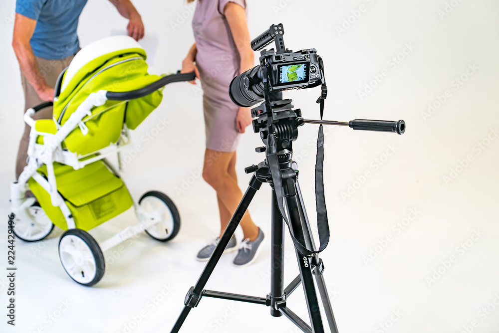 camera is on a tripod and focused on a young family with a stroller on a white background