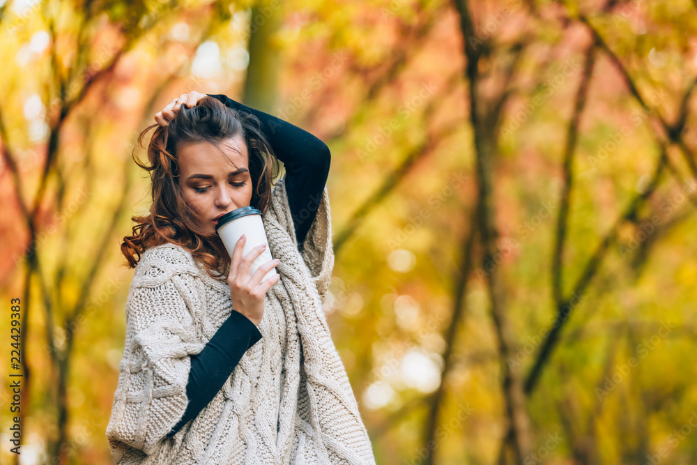 一个沉思的女人拿着一杯咖啡站在公园里，把她的卷发拉直。