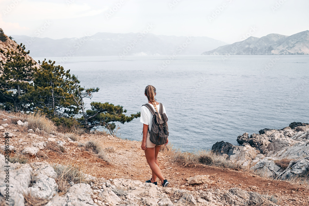 背着背包的徒步女孩沿着海湾徒步旅行