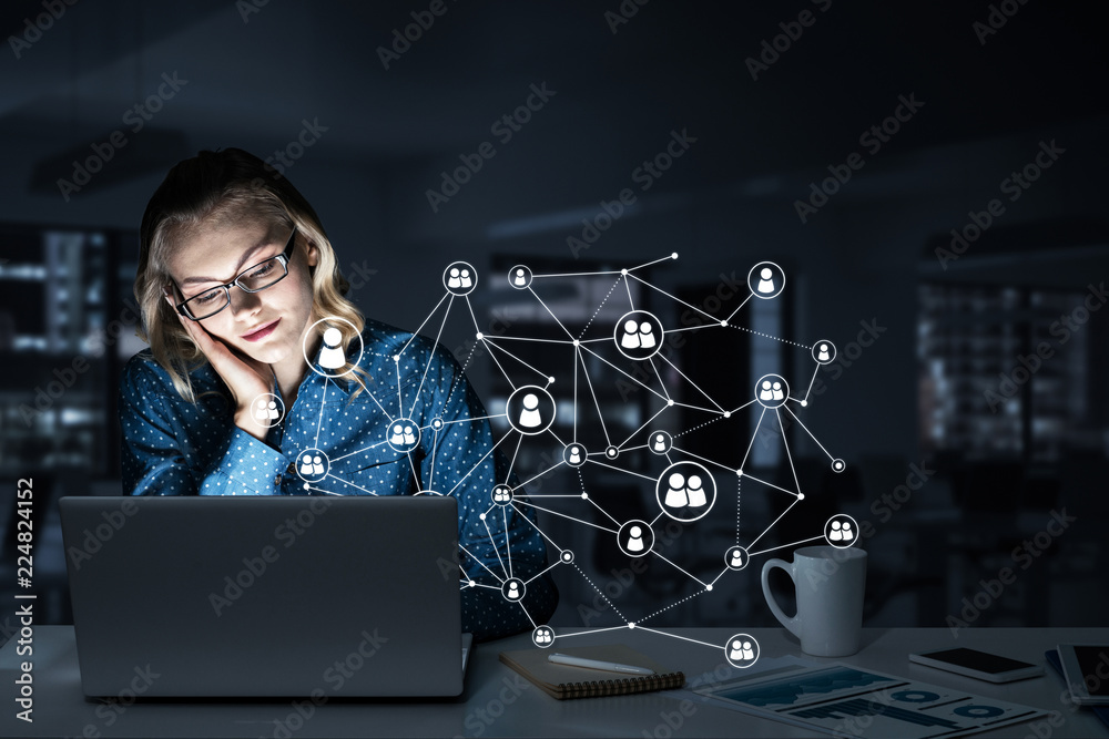 Attractive blonde wearing glasses in dark office using laptop. M