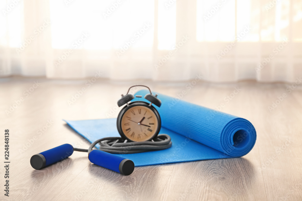 Yoga mat with jumping rope and alarm clock on floor