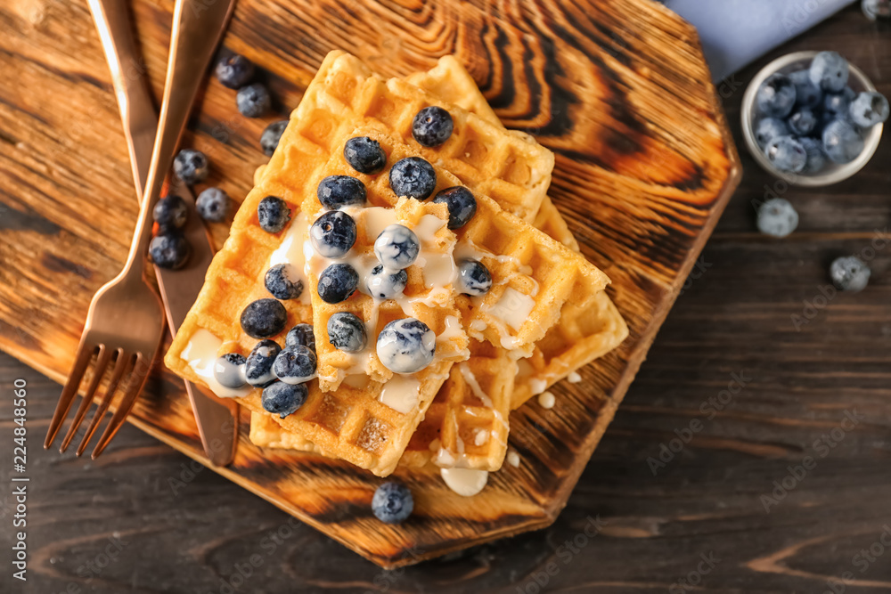 Delicious waffles with sauce and blueberries on wooden board