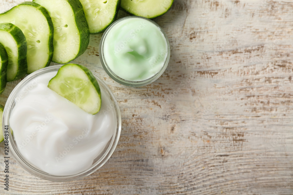 Bowls with cucumber body cream on wooden table, top view