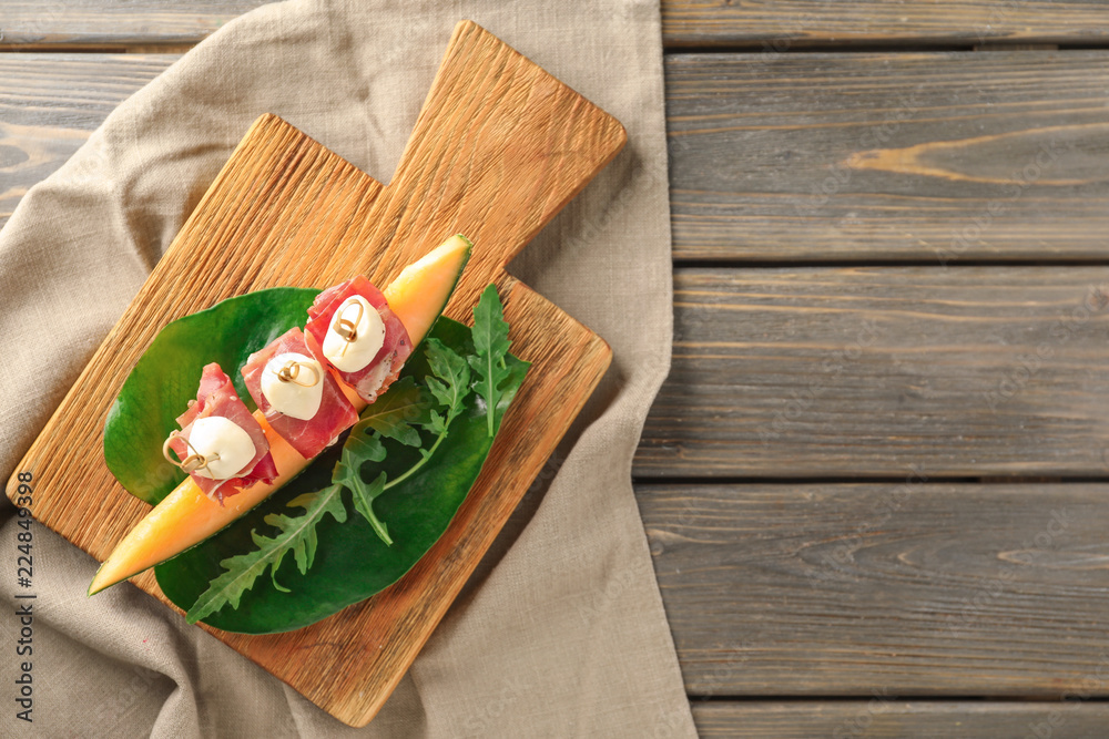 Delicious canape with melon, prosciutto and mozzarella on wooden board, top view