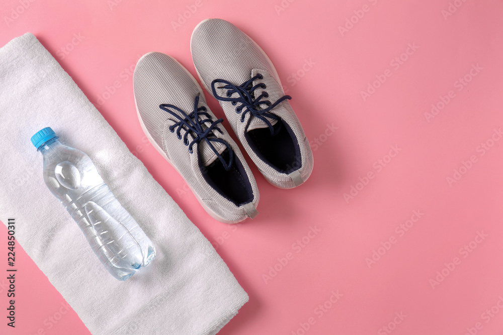 Clean soft towel with sports shoes and bottle of water on color background