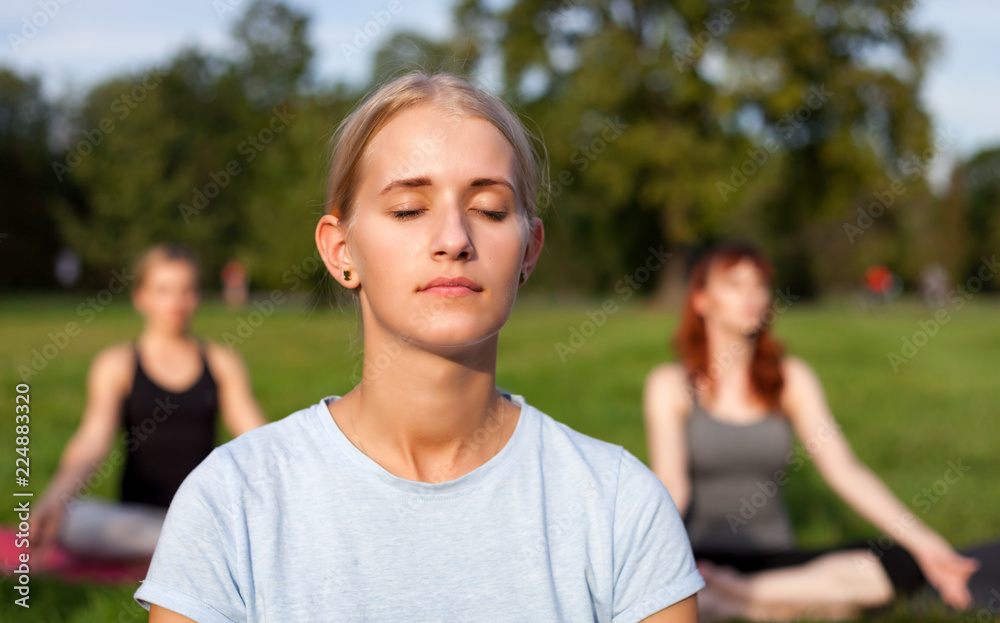 Yoga in the park, young woman doing exercises with group of mixed age people