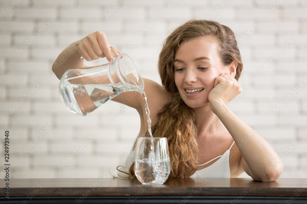 Young woman pouring water from jug into glass in the room