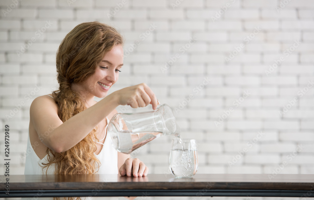 年轻女子将水壶里的水倒进房间的玻璃里