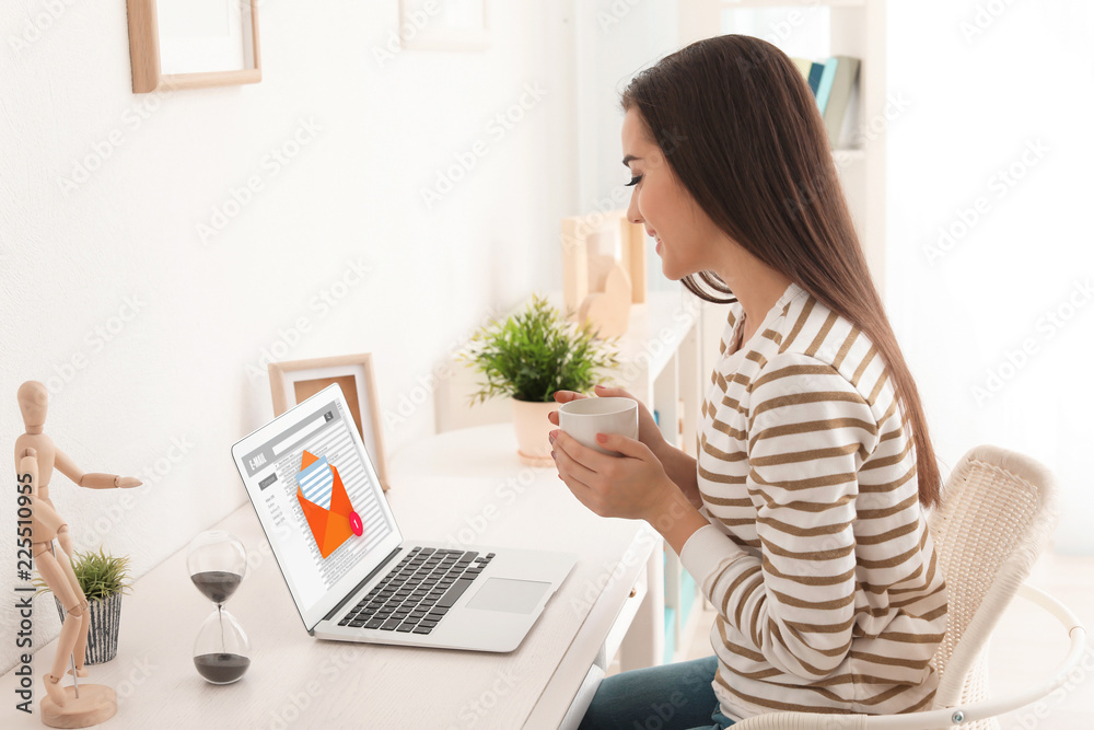 Young woman drinking coffee while working with modern laptop at table