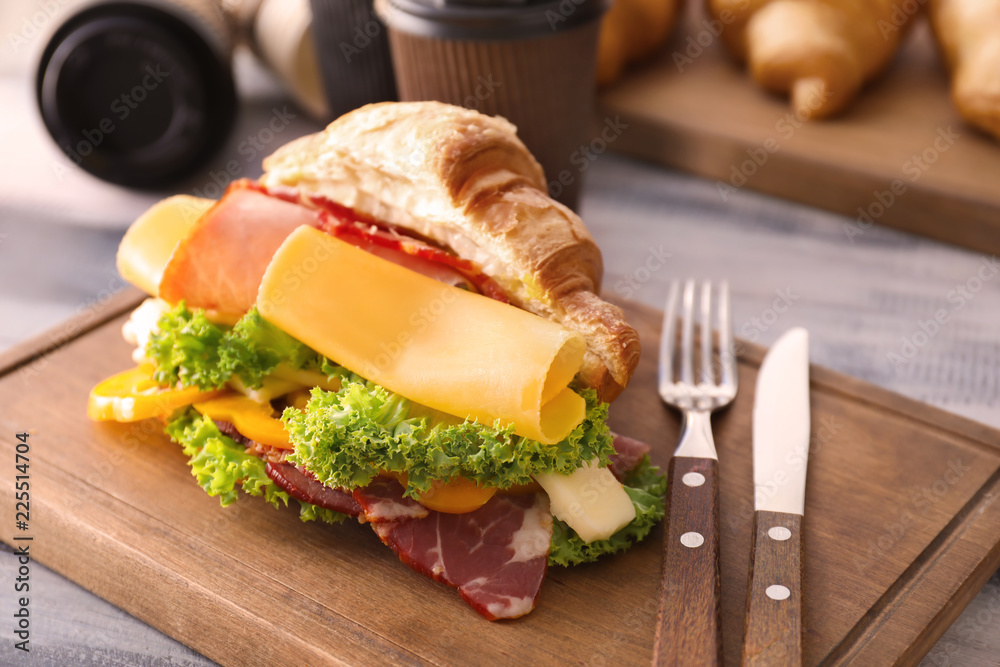 Tasty croissant sandwich with meat on wooden board