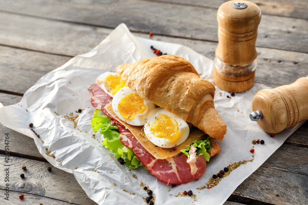 Tasty croissant sandwich with meat on parchment