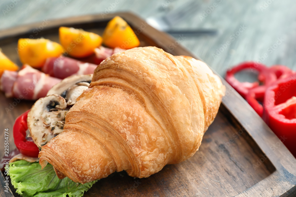 Tasty croissant sandwich with meat on wooden board, closeup