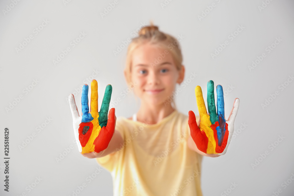 Cute little girl with hands in paint on light background