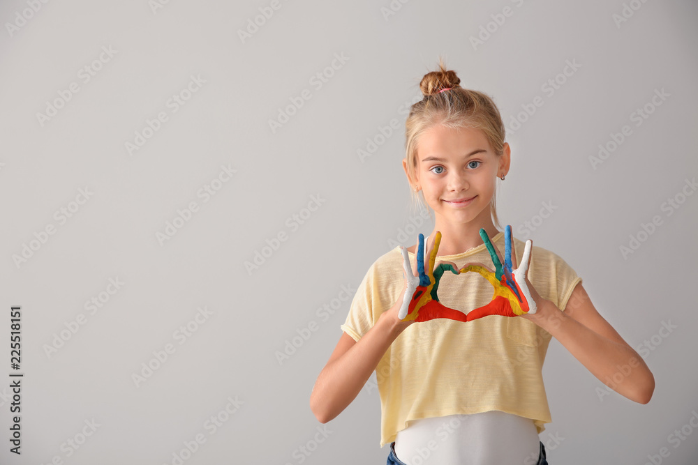 Cute little girl making heart with hands in paint on light background