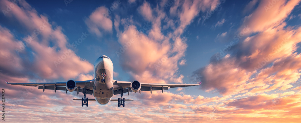 Landing airplane against colorful sky at sunset. Landscape with aircraft is flying in the blue sky w