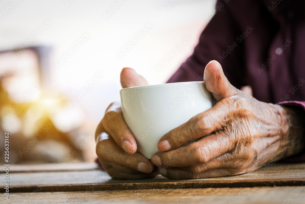 木头桌子上拿着一杯咖啡的老人的手。画风