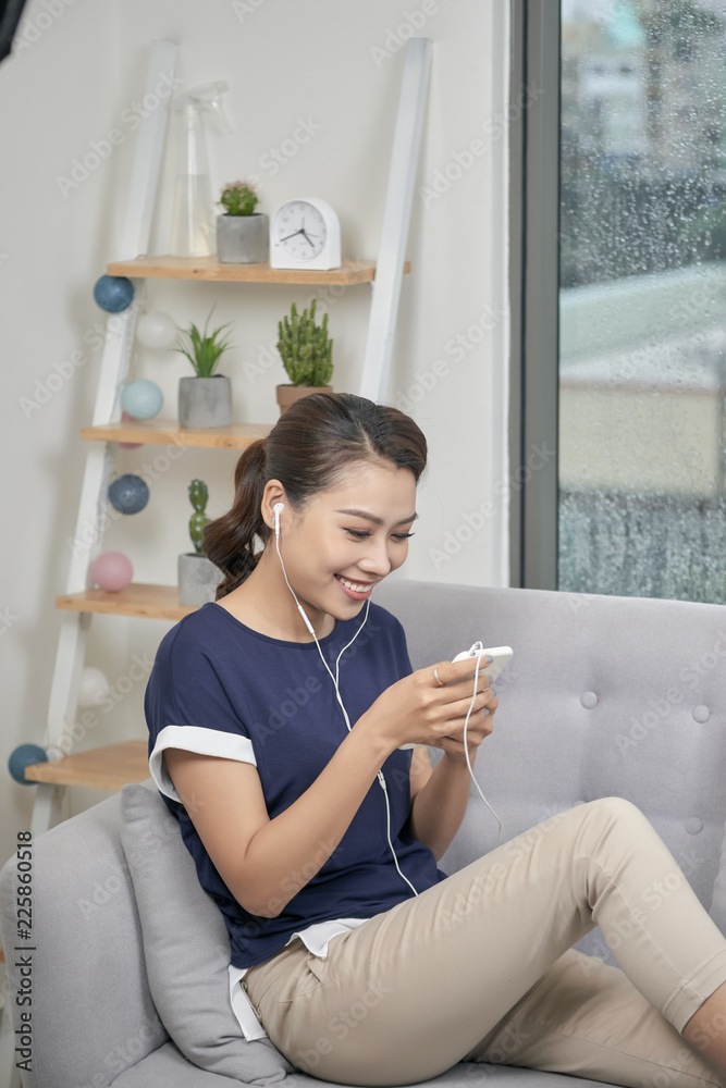 微笑的女孩在家里放松，戴着耳机听音乐。带着ph的快乐年轻女士的室内照片