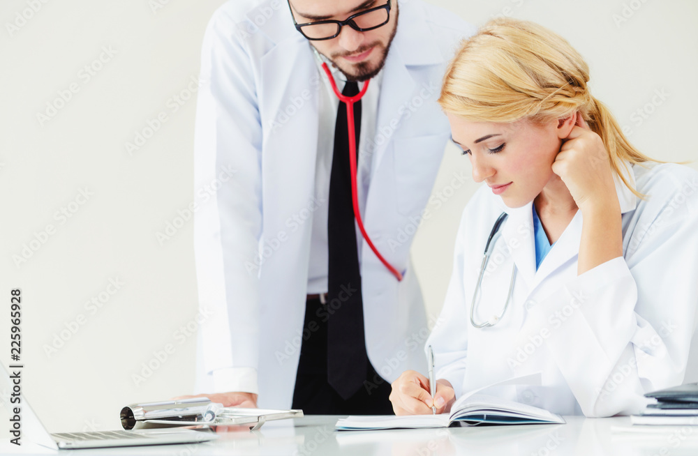 Doctor writes report at desk with another doctor.