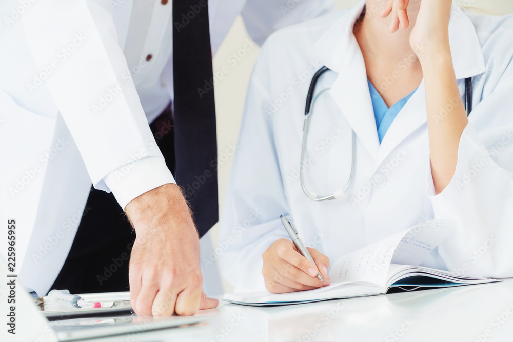 Doctor writes report at desk with another doctor.