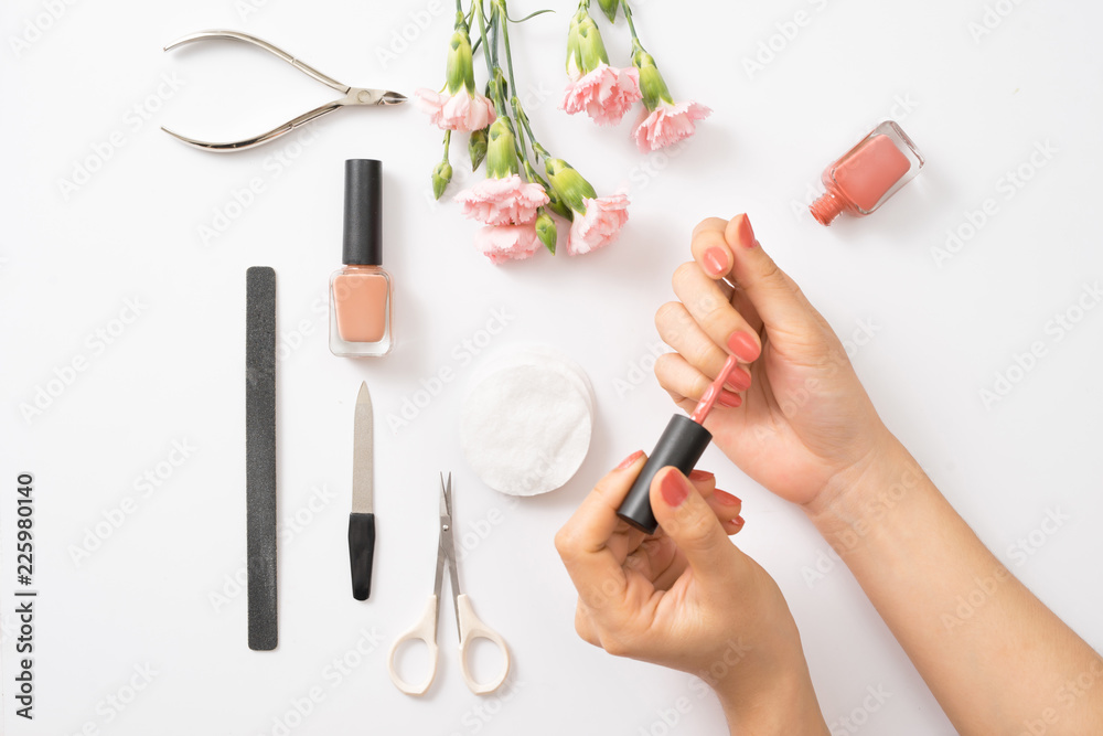 Female hands applying purple nail polish on wooden table with towel and nail set