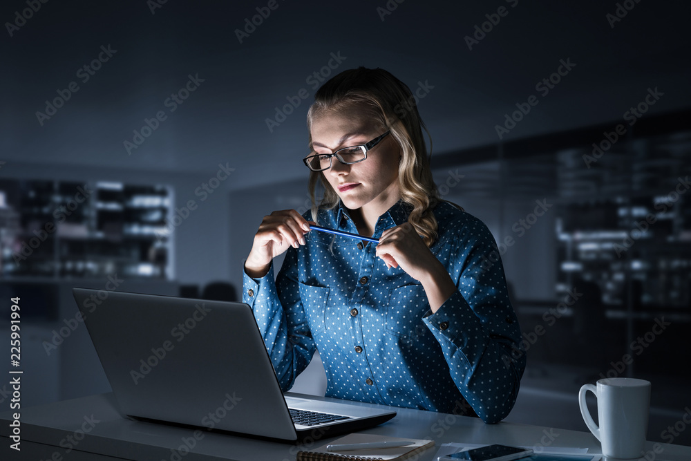 Attractive blonde working on laptop in dark office. Mixed media